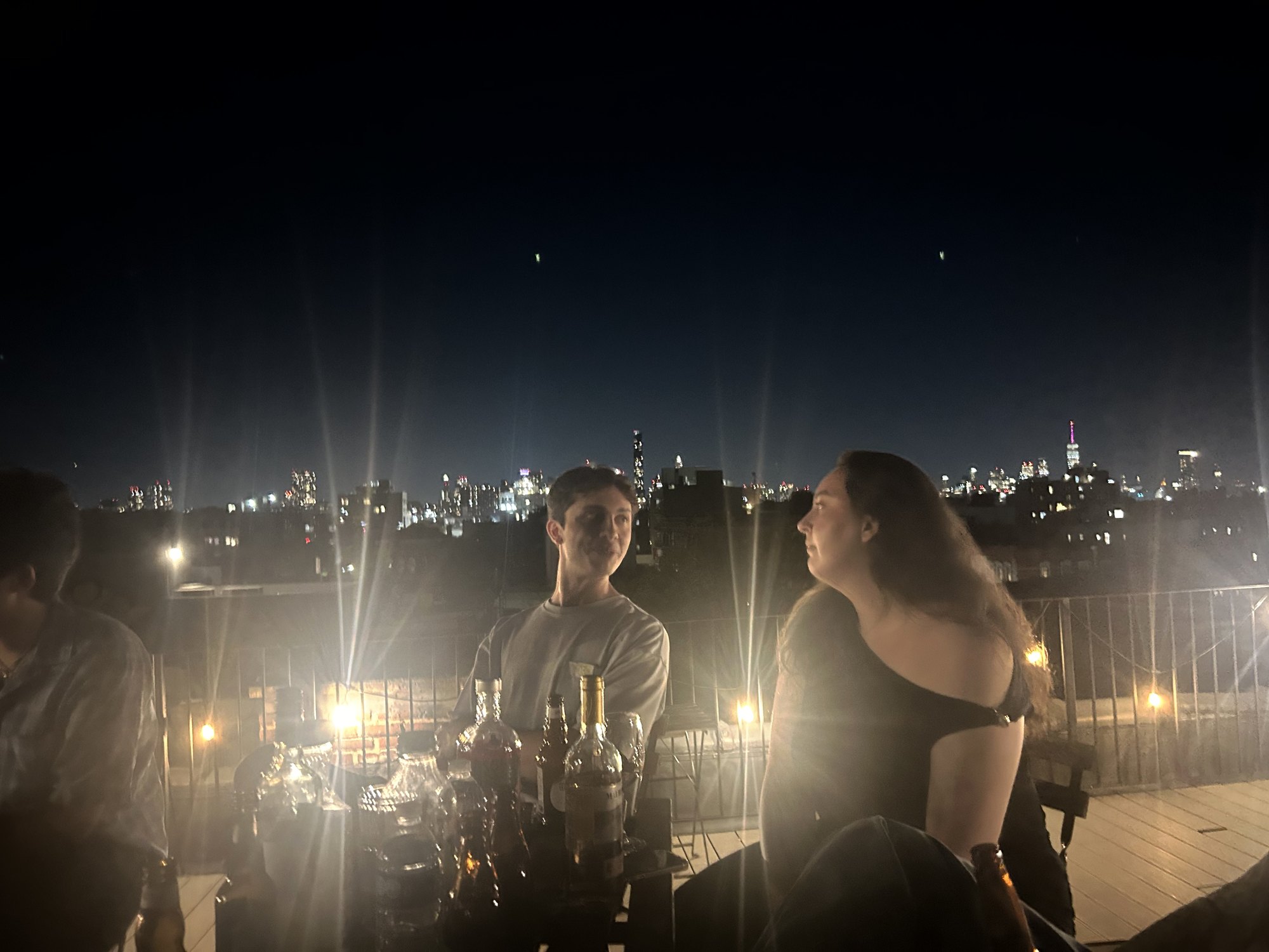 Two guests mid-conversation beside the table, string lights flaring across the frame