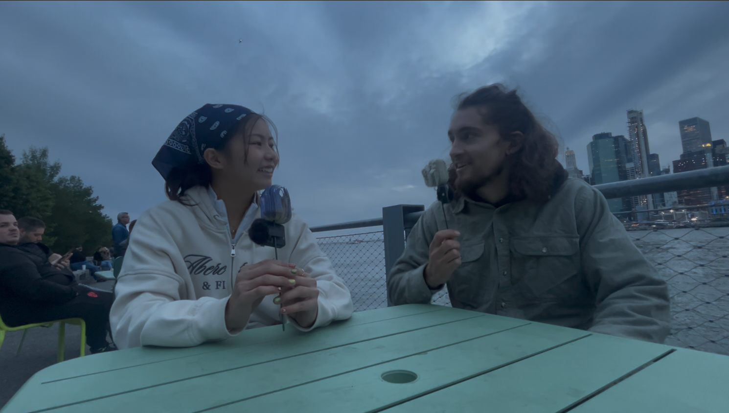 James, hair down, interviewing Kate Lau at a picnic table with the Manhattan skyline behind them